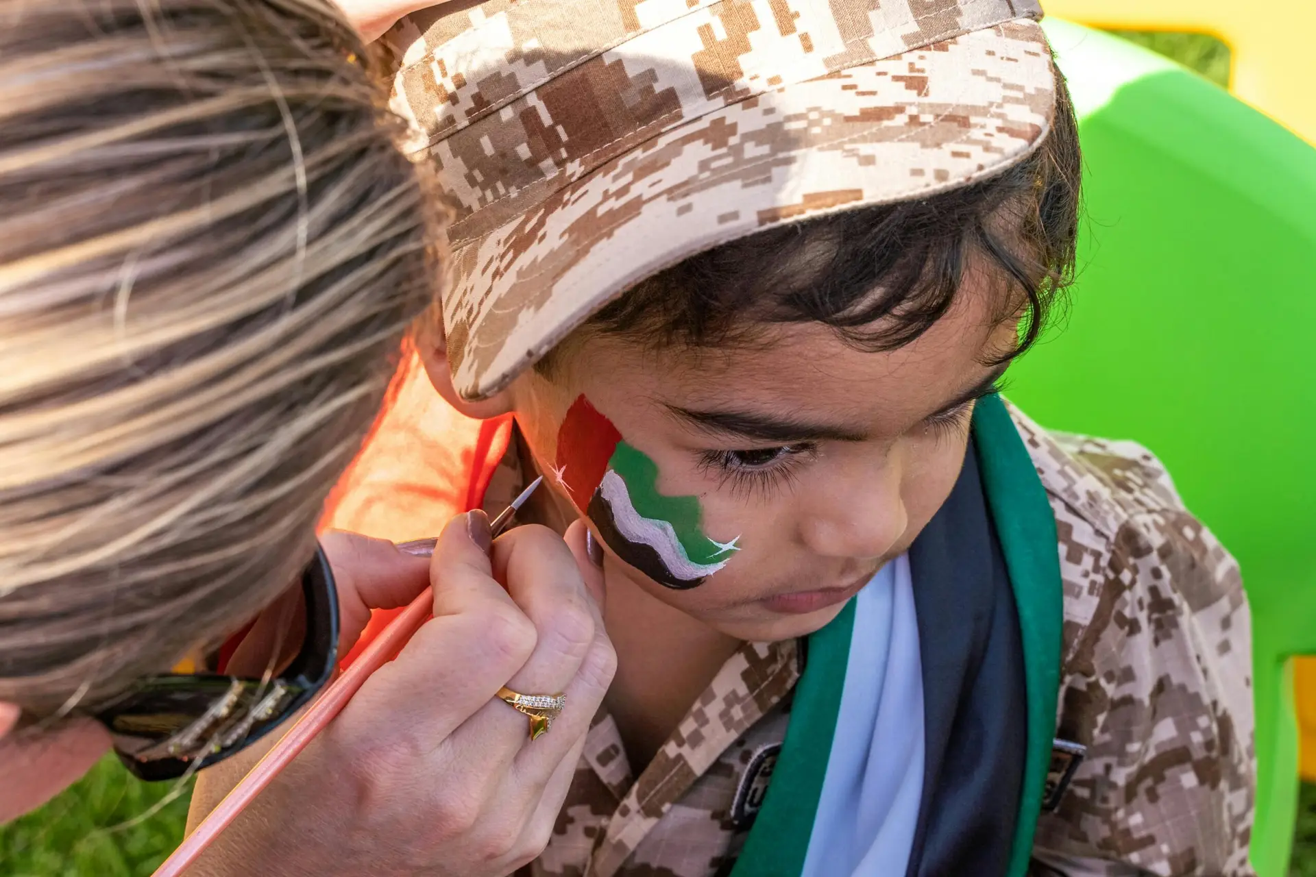 A close-up of a child in UAE flag face paint during a national event in Dubai outdoors.