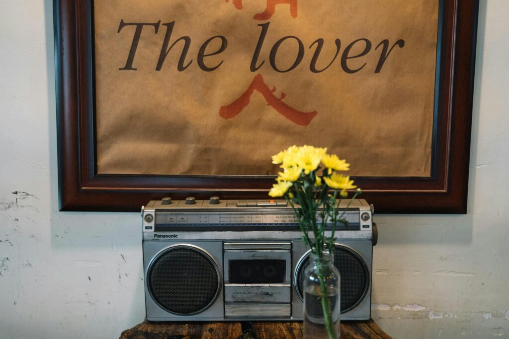 Retro setup with a classic boombox, nostalgic poster, and yellow flowers in a vase on a wooden table.